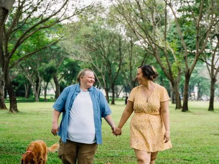 An older couple holding hands while walking two small dogs across a park lawn